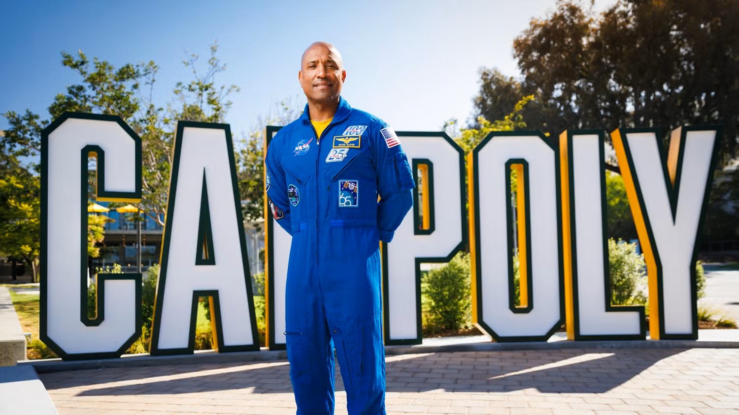 A man in a blue jumpsuit stands in front of giant letters that read "CAL POLY"
