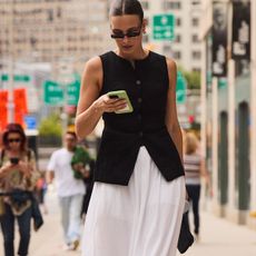Woman in a black vest and a white skirt looking at a phone