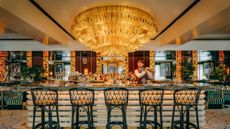 A huge golden chandelier shines over a marbled bar where a man shakes a cocktail at high speed