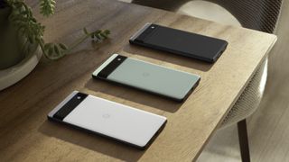 Three Google Pixel 6a units in different colors, lying on a wooden table