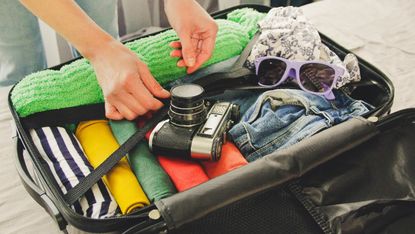 Person packing suitcase with sunglasses and binoculars