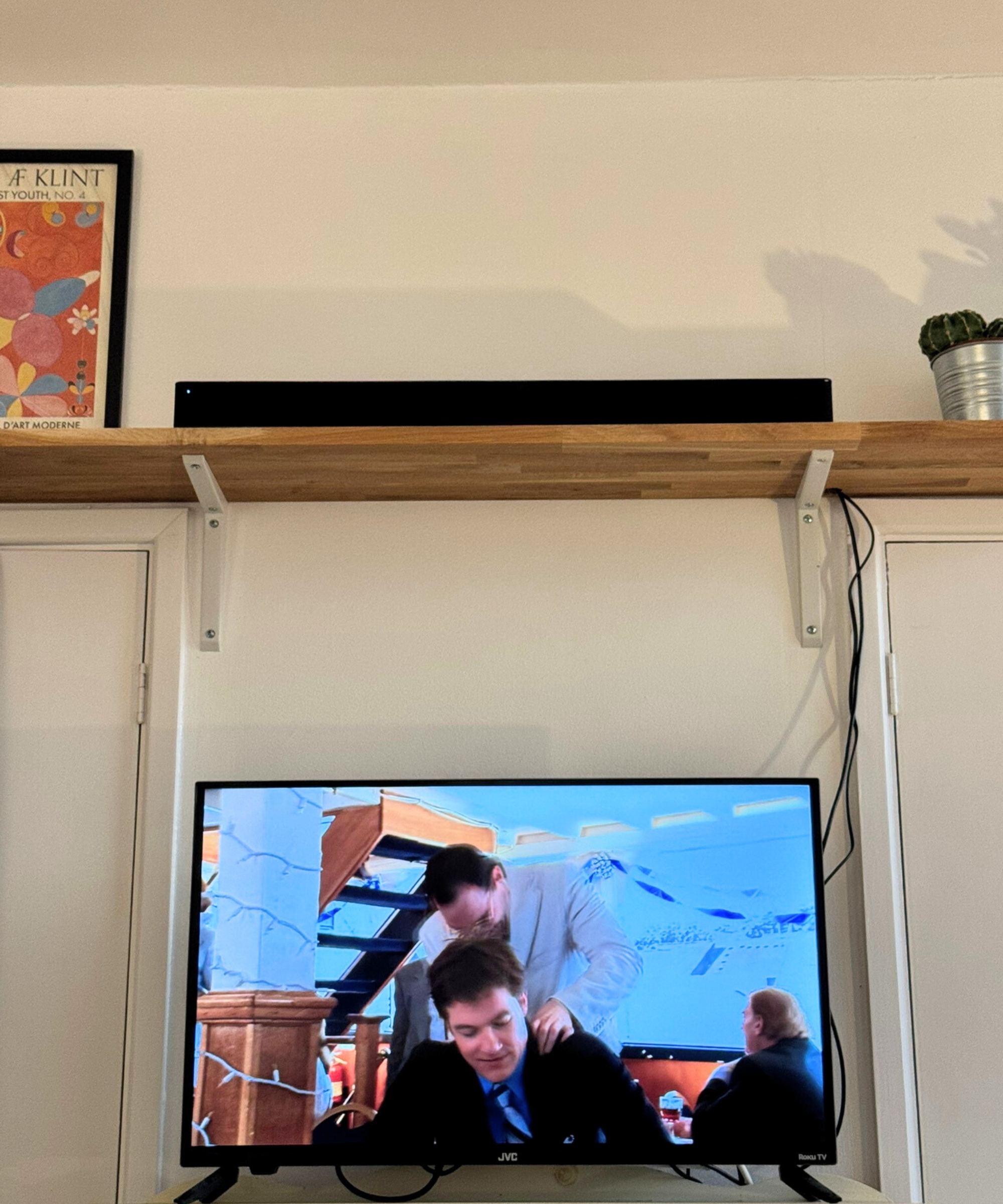 Hisense HS2100 soundbar on wooden shelf next to potted cactus and framed print, above TV showing Arrested Development.