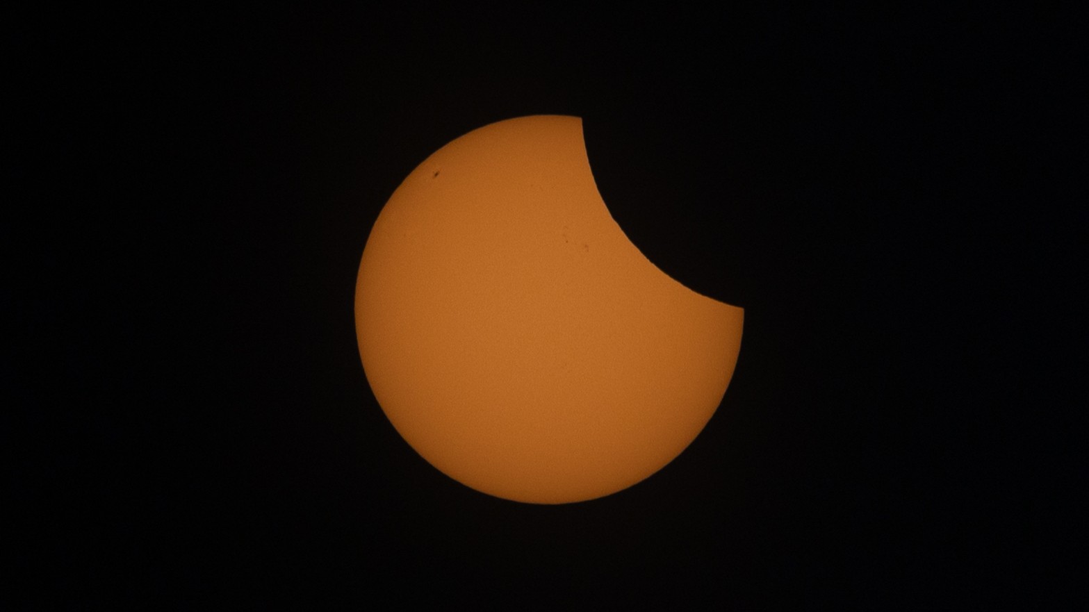 a partially eclipses sun with the upper right portion appearing missing, it is actually just being covered by the moon.