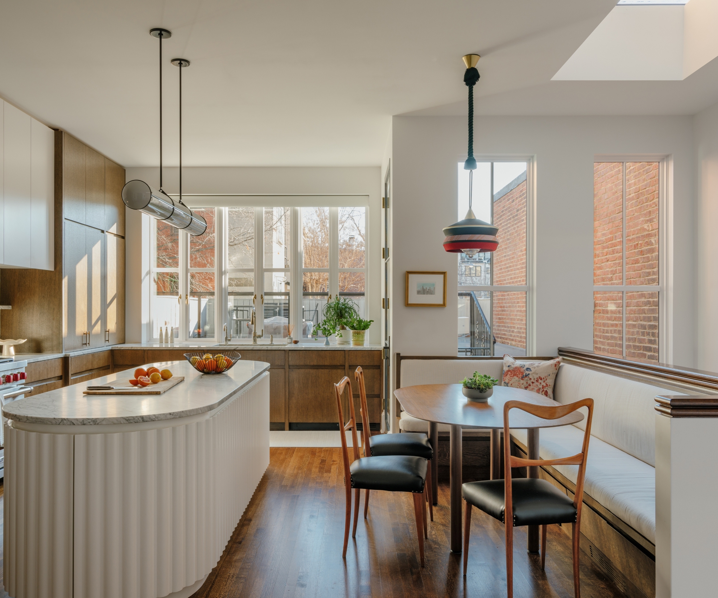 A light neutral kitchen with a cream island, wooden perimeter cabinets, and a built-in banquette seating area with cream upholstery and an oval wooden table