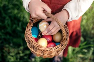 A young child holding Easter eggs in a small wicker basket.