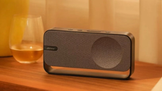 The Bose SoundLink Home on what looks like a bedside table with a clear glass of liquid beside it.