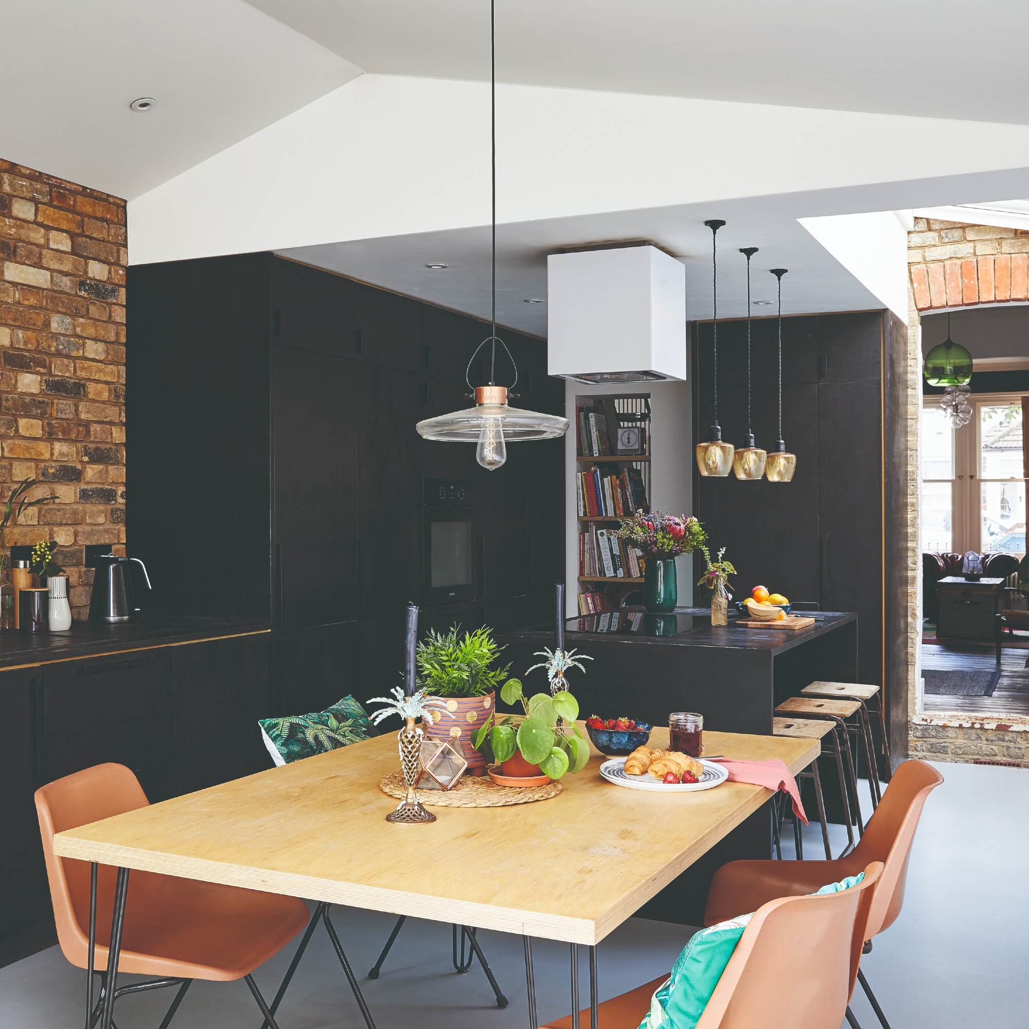 A black kitchen with a kitchen island and three pendant lights positioned above with a connected dining area and a pendant light hung above the table
