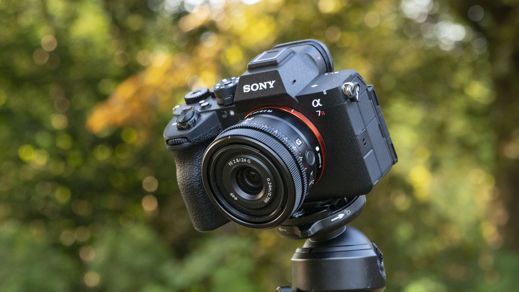 The Sony A7R VI camera with 24mm f/2.8 lens attached, it's mounted to a tripod outdoors, there's a natural background