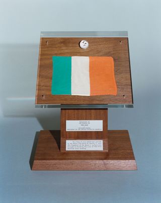 a wooden podium displaying a four small pebbles inside a clear lucite sphere and a green, white and orange striped flag.