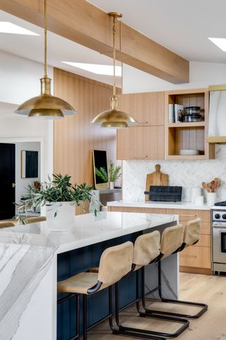 white and wood kitchen with blue underside breakfast bar/kitchen island, bar stools, gold pendant lights, wooden cabinets, marble island