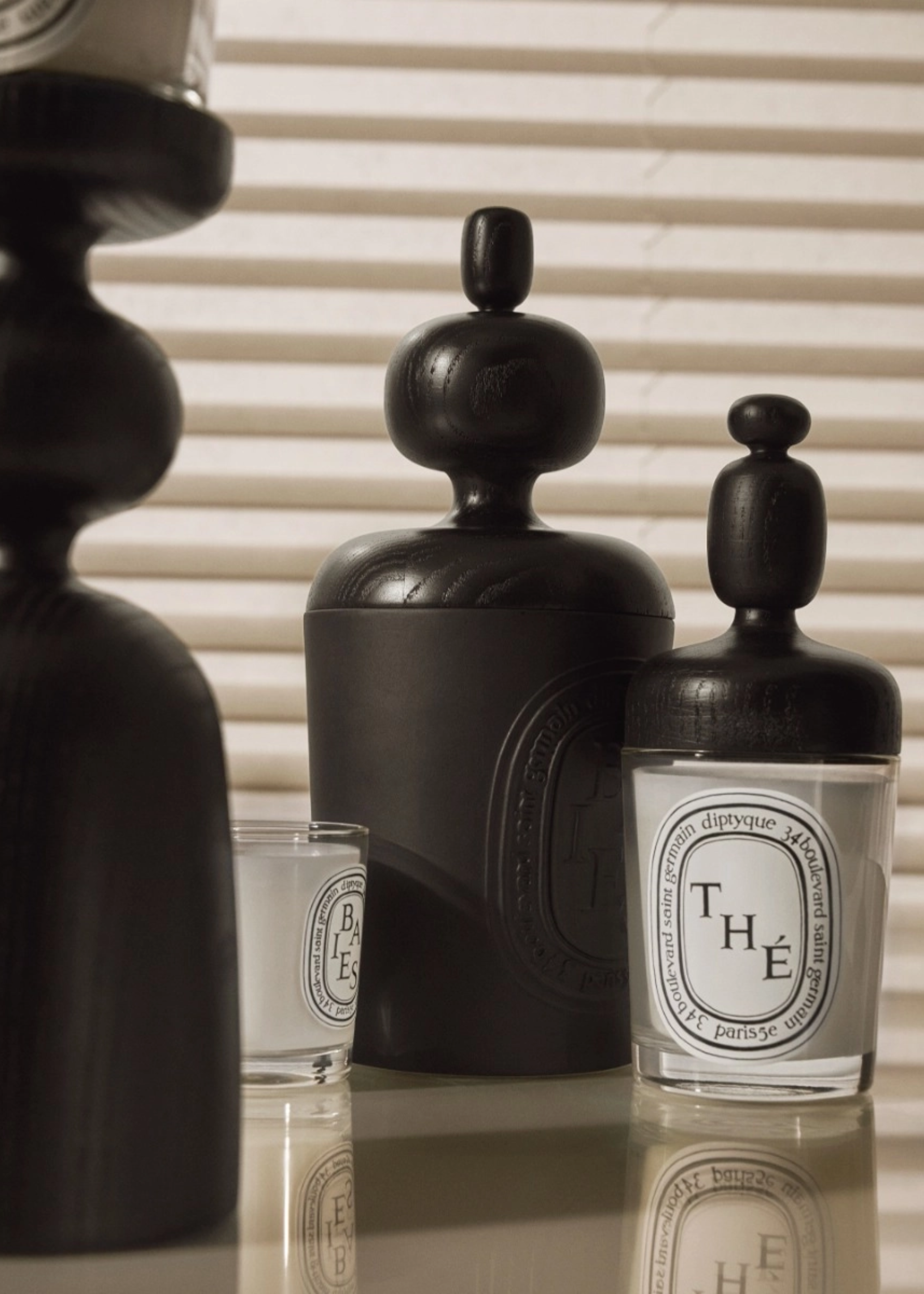 A couple of Diptyque glass candles with black wood structured lids