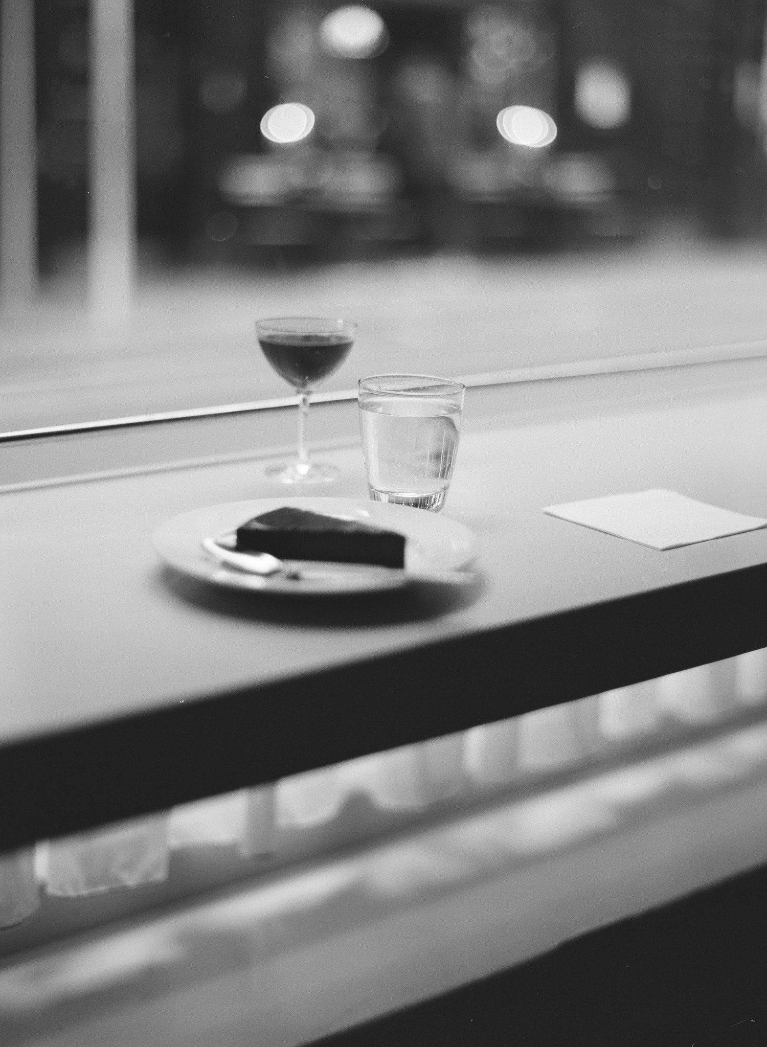 A black-and-white film shot of a cake, a glass of water, and a drink served in a Martini-style gobblet.