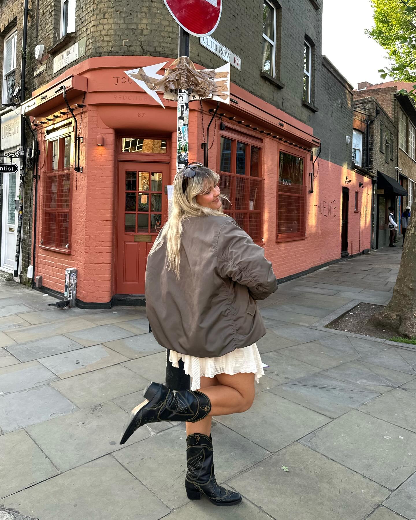 An image of @gracealexandriaa wearing cowboy boots with a bomber jacket and handkerchief skirt.