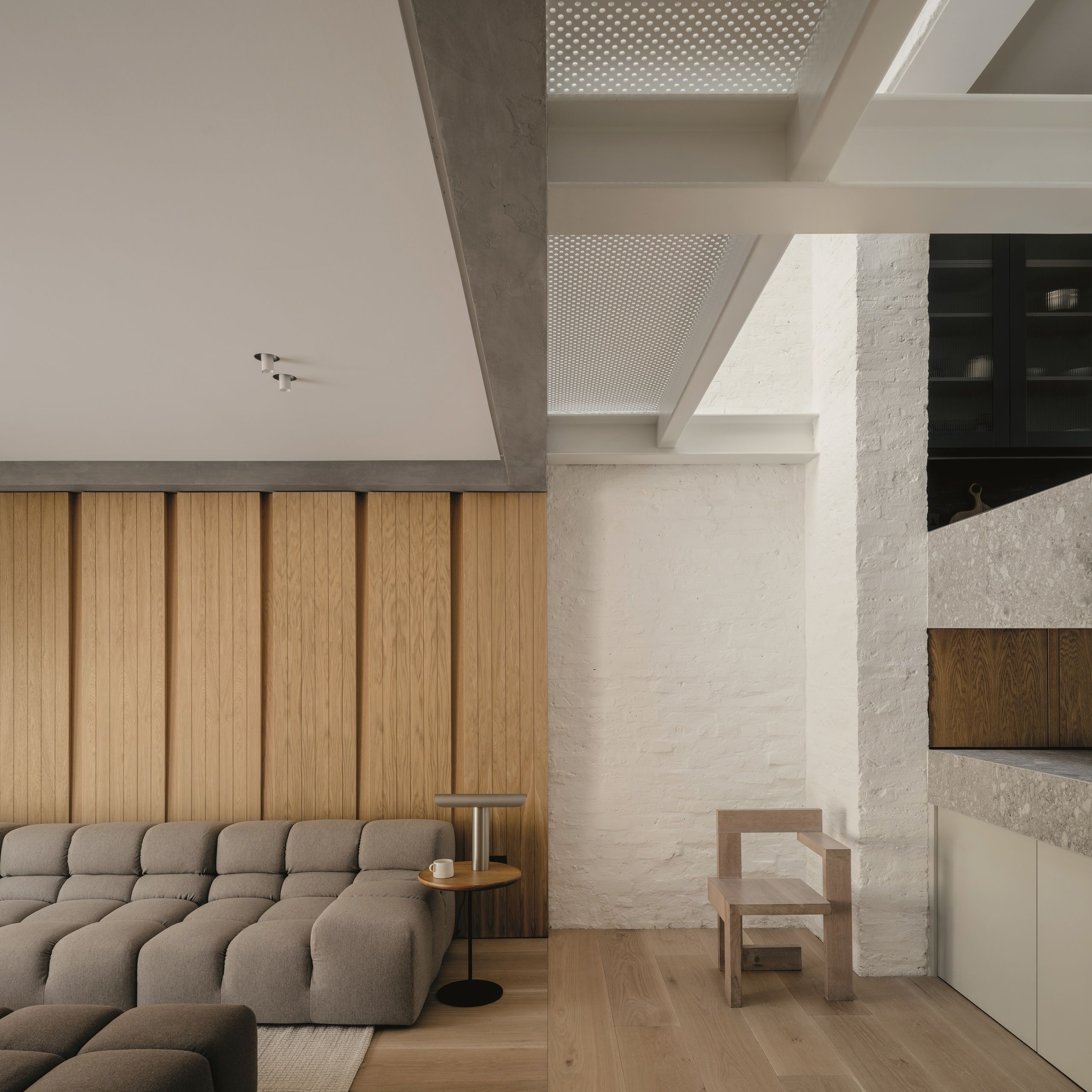 modern extension with perforated steel ceiling, wood panelled walls, painted white brick walls, gray sofa and ottoman
