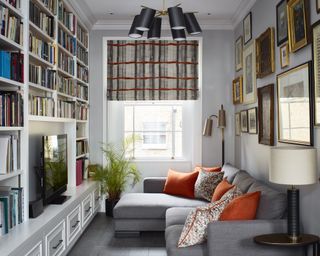A snug with a wall of bookshelves, gallery wall and grey corner sofa with orange cushions