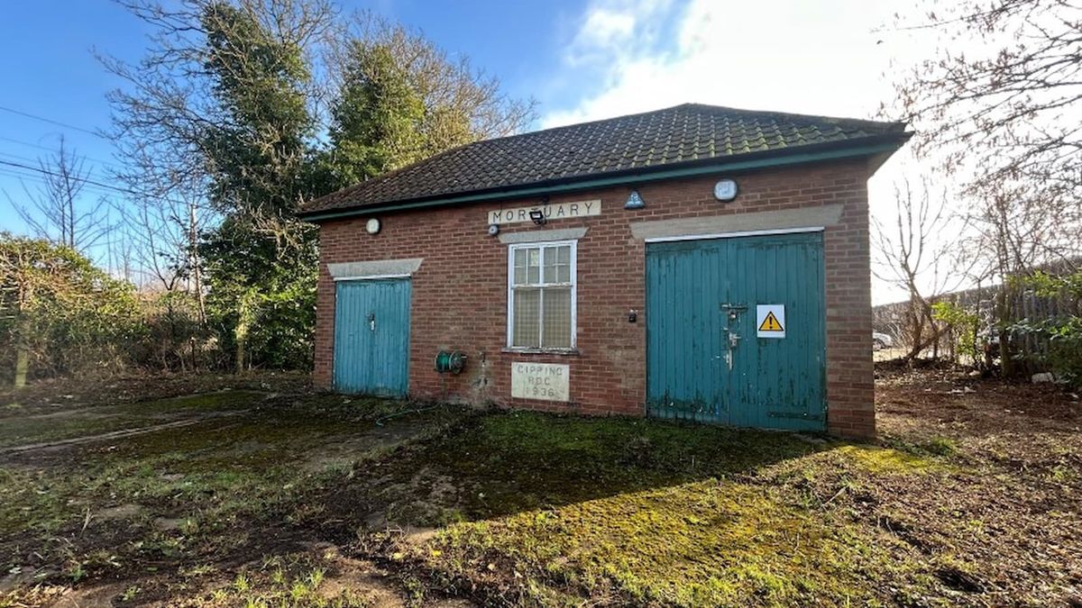 A small former mortuary on a plot of land with green door and a brick structure