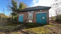 A small former mortuary on a plot of land with green door and a brick structure