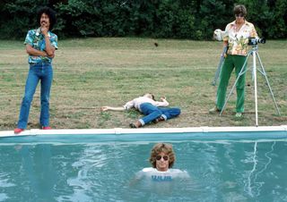 Be-Bop Deluxe photographed by a swimming pool, with one member submerged in the water