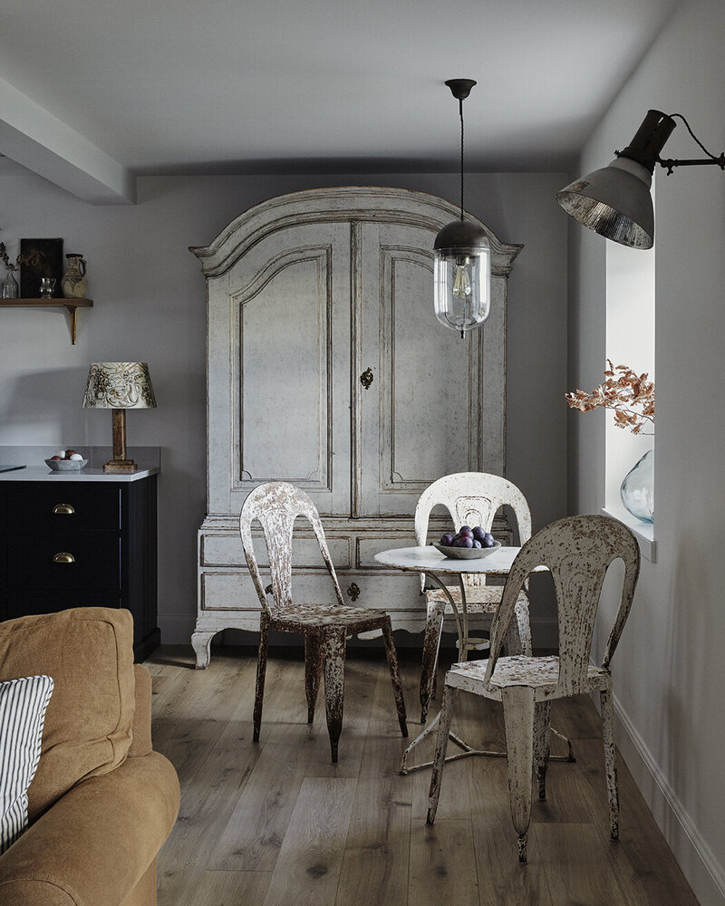 A quirkily decorated, shabby-chic farmhouse features distressed iron chairs and wooden cabinets, industrial lighting, wooden floors, and sleek surfaces.