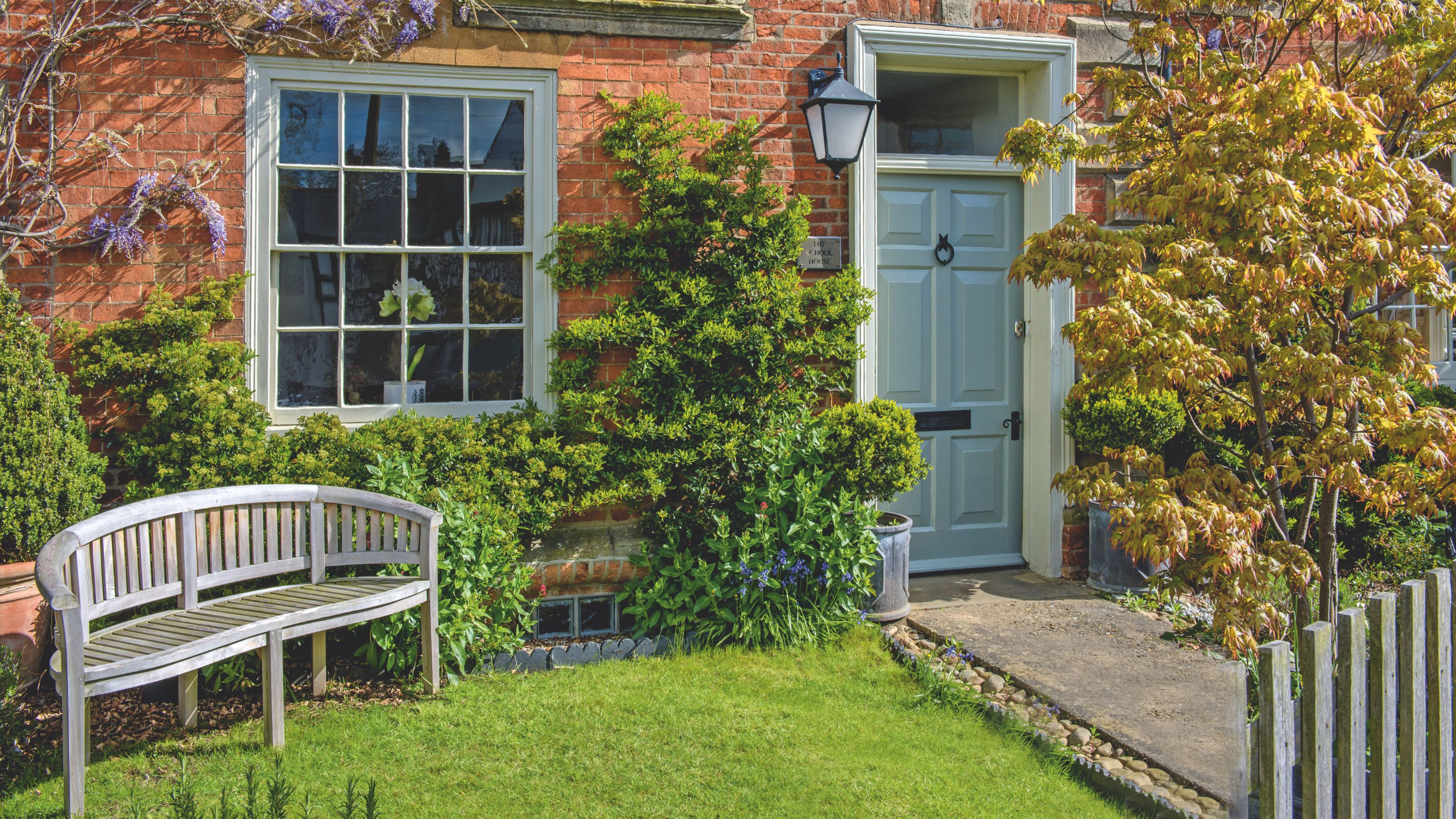 Front of a period house, with a blue front door and a wooden bench on the grass in the front garden