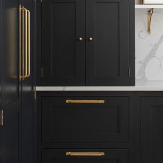 Black kitchen with white worktops and brass t-bar cabinet handles.