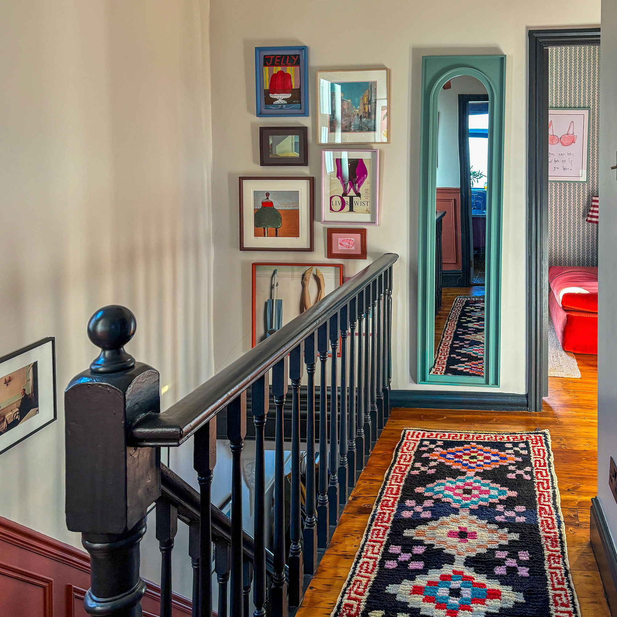 Upper landing with colourful folksy rug, turquoise framed full length mirror and gallery wall at top of staircase
