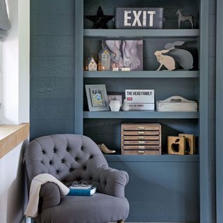 Grey armchair in front of teal panelled bookcase shelving unit