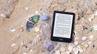 The Kobo Clara 2E ereader on the beach with recyclable plastic around it