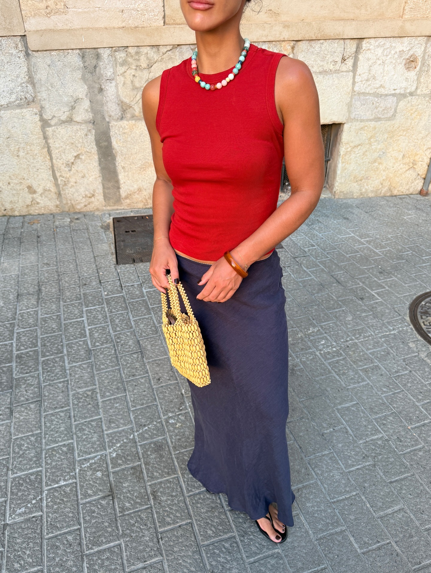 Woman in a red tank, beaded necklace, and linen skirt.