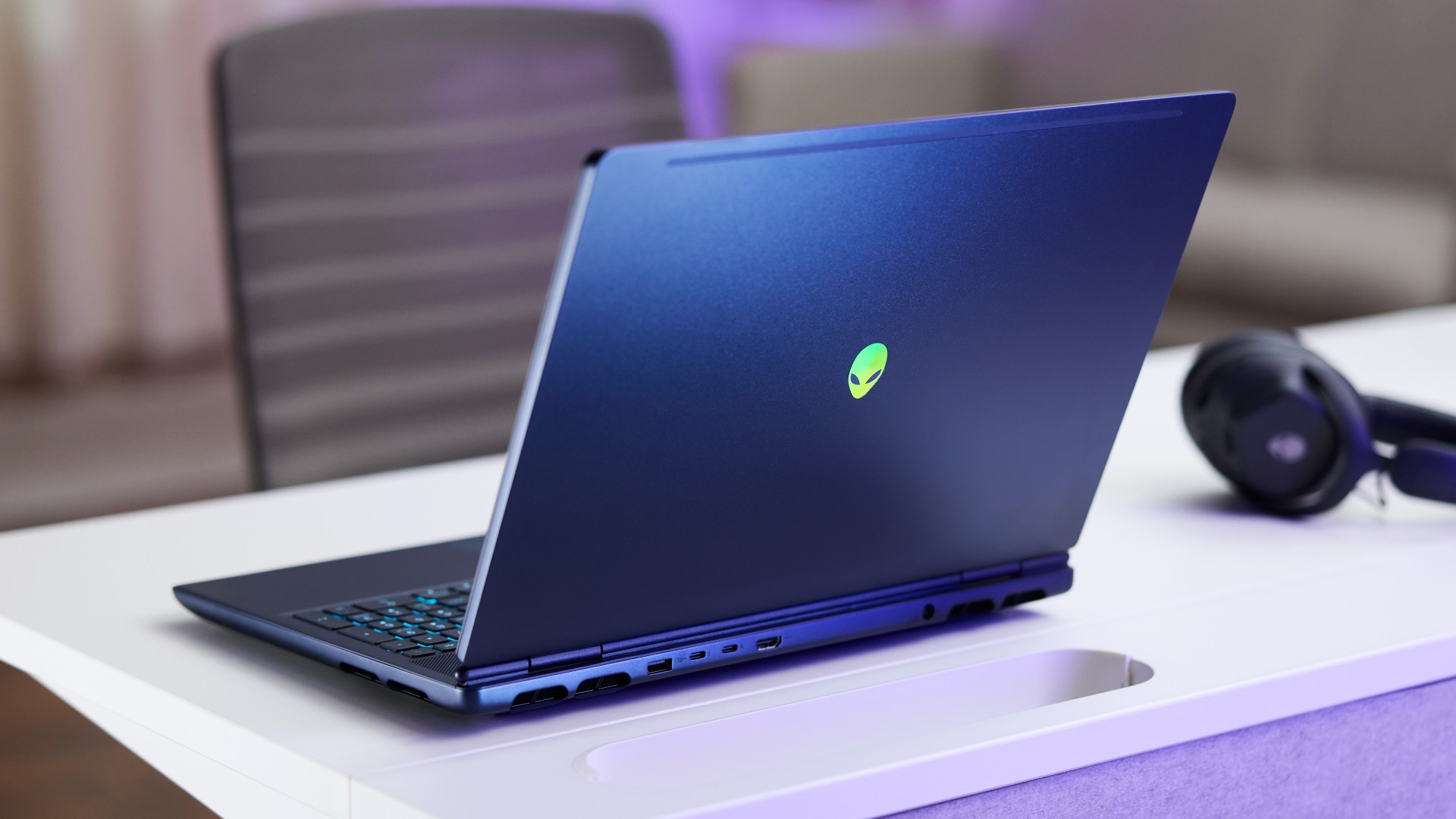 Rear view of the top lid of the Alienware Aurora 16X gaming laptop with brand logo illuminated in green RGB while it sits on a white desk