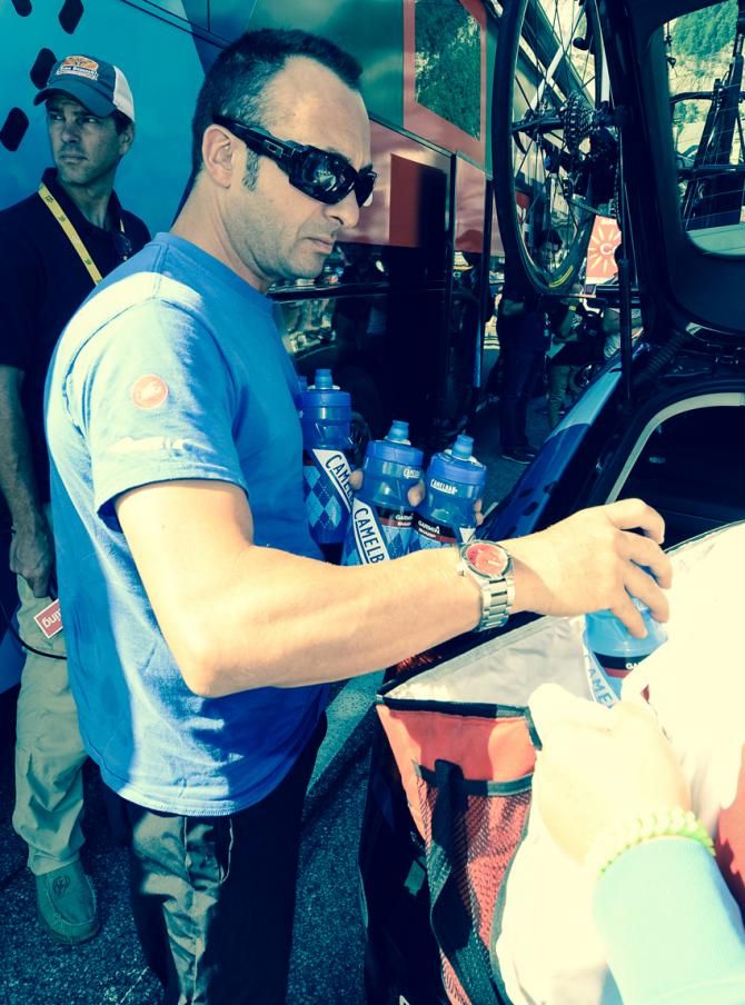 Frankie Andreu hangs in the background as a soigneur gathers the water bottles for the team.