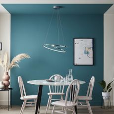4 seat white chairs and white dining table with black legs in front of a dynamic blue feature wall, with a silver feature pendant light hanging above