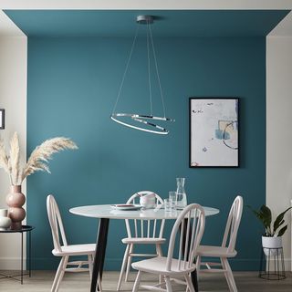 4 seat white chairs and white dining table with black legs in front of a dynamic blue feature wall, with a silver feature pendant light hanging above