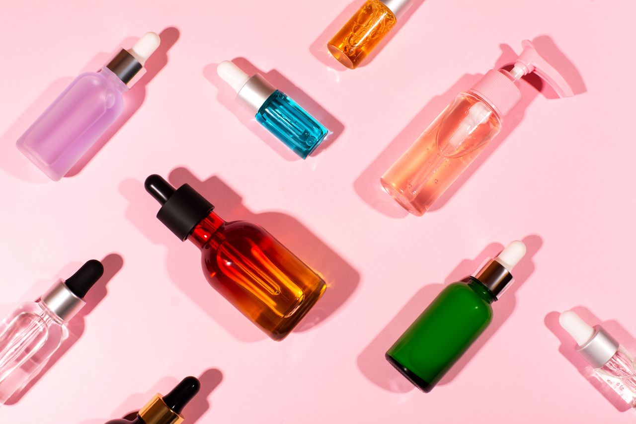 A pink background with a selection of skincare products in various glass bottles with droppers