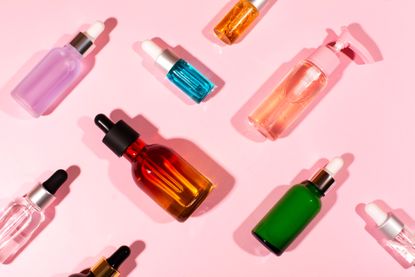 A pink background with a selection of skincare products in various glass bottles with droppers
