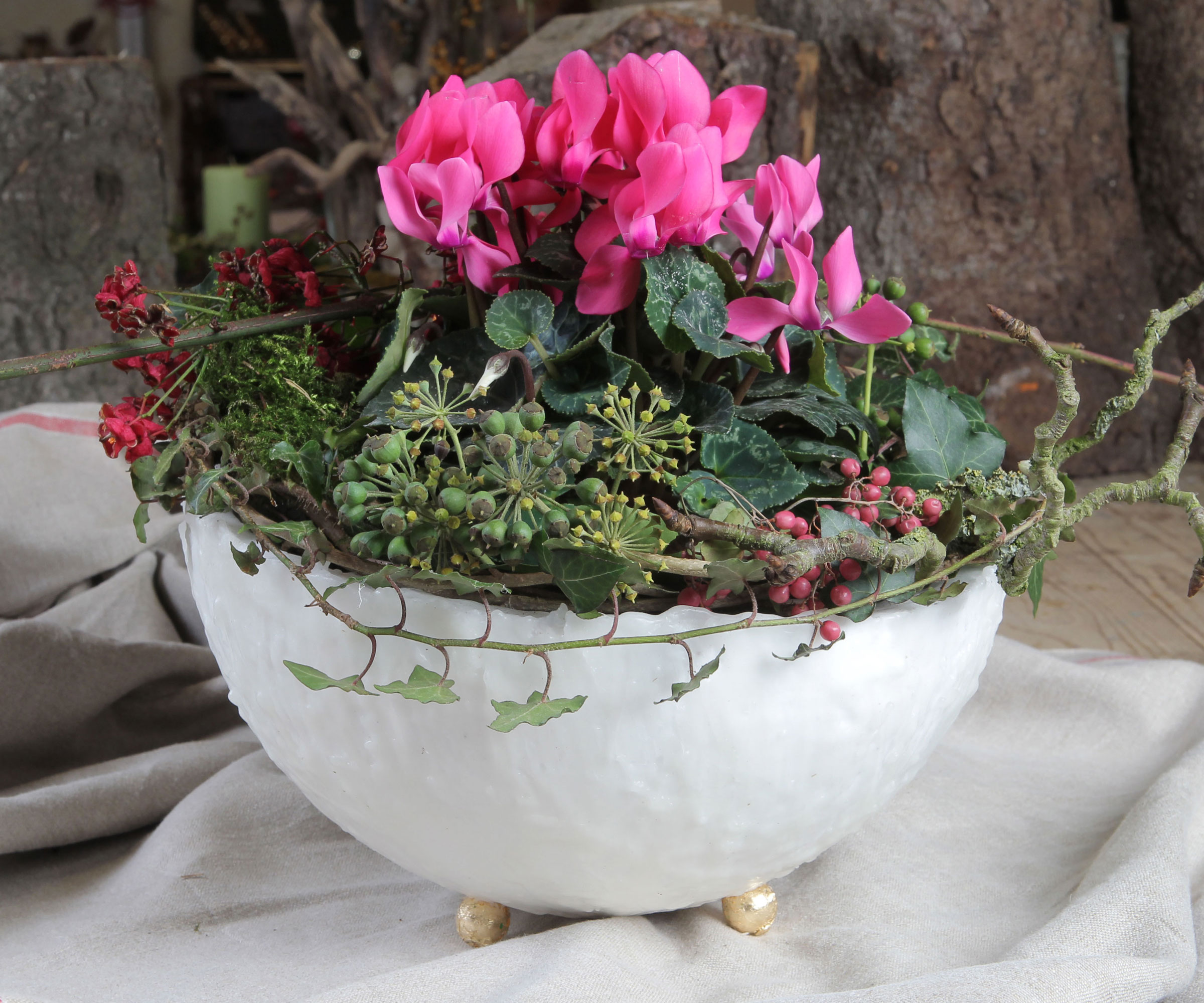 ceramic bowl festive table decoration with pink cyclamen, foliage and berries