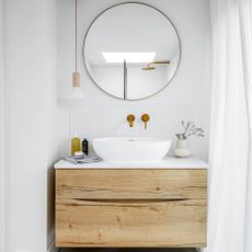 Small white bathroom with wooden floating vanity unit and large round mirror on wall 