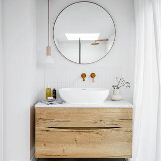 Small white bathroom with wooden floating vanity unit and large round mirror on wall