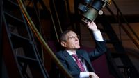 a man in a suit peers up into a large telescope