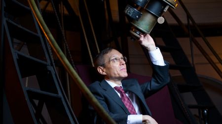 a man in a suit peers up into a large telescope