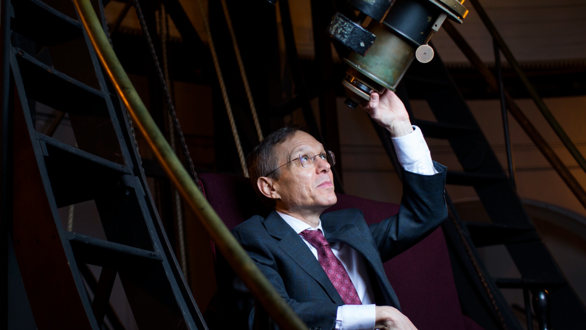 a man in a suit peers up into a large telescope