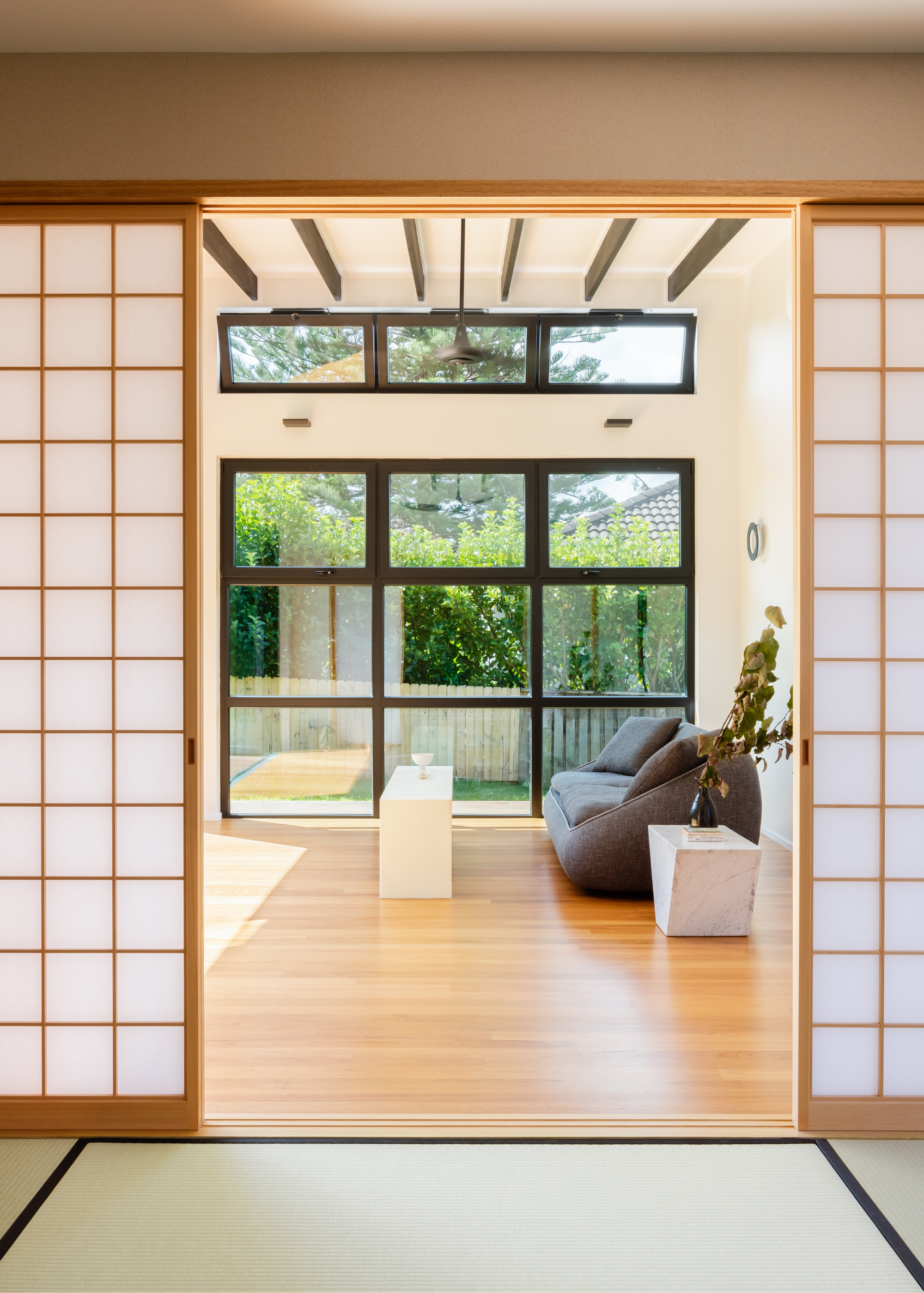 A set of wood and rice paper doors leading to a bright living room with a gray couch, a marble side table, and a white coffee table
