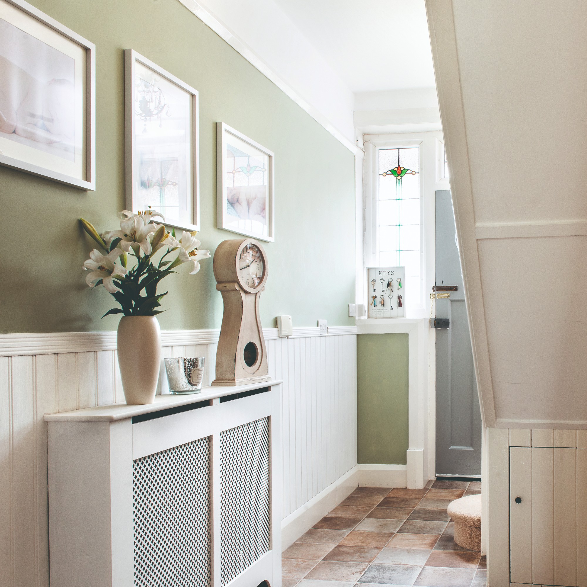 A hallway with a dado rail along the wall with the top half painted in sage green and the bottom covered in off-white wall panelling