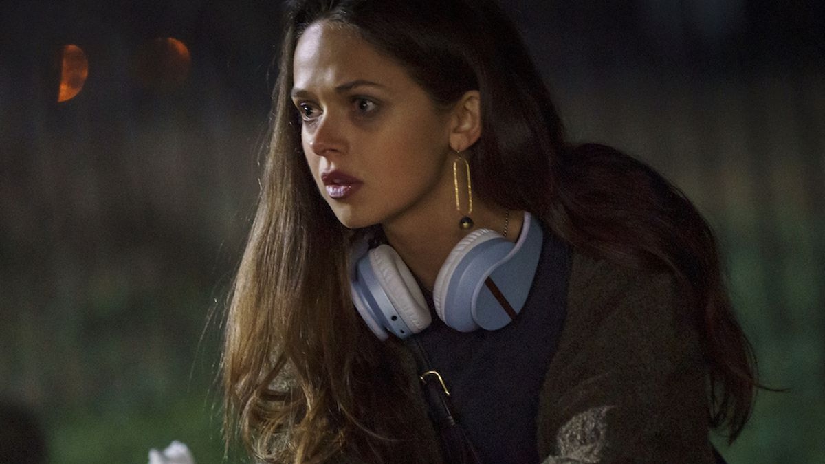 Alyssa Jirrels at a grave site looking concerned with headphones around her neck in Mayfair Witches Season 2