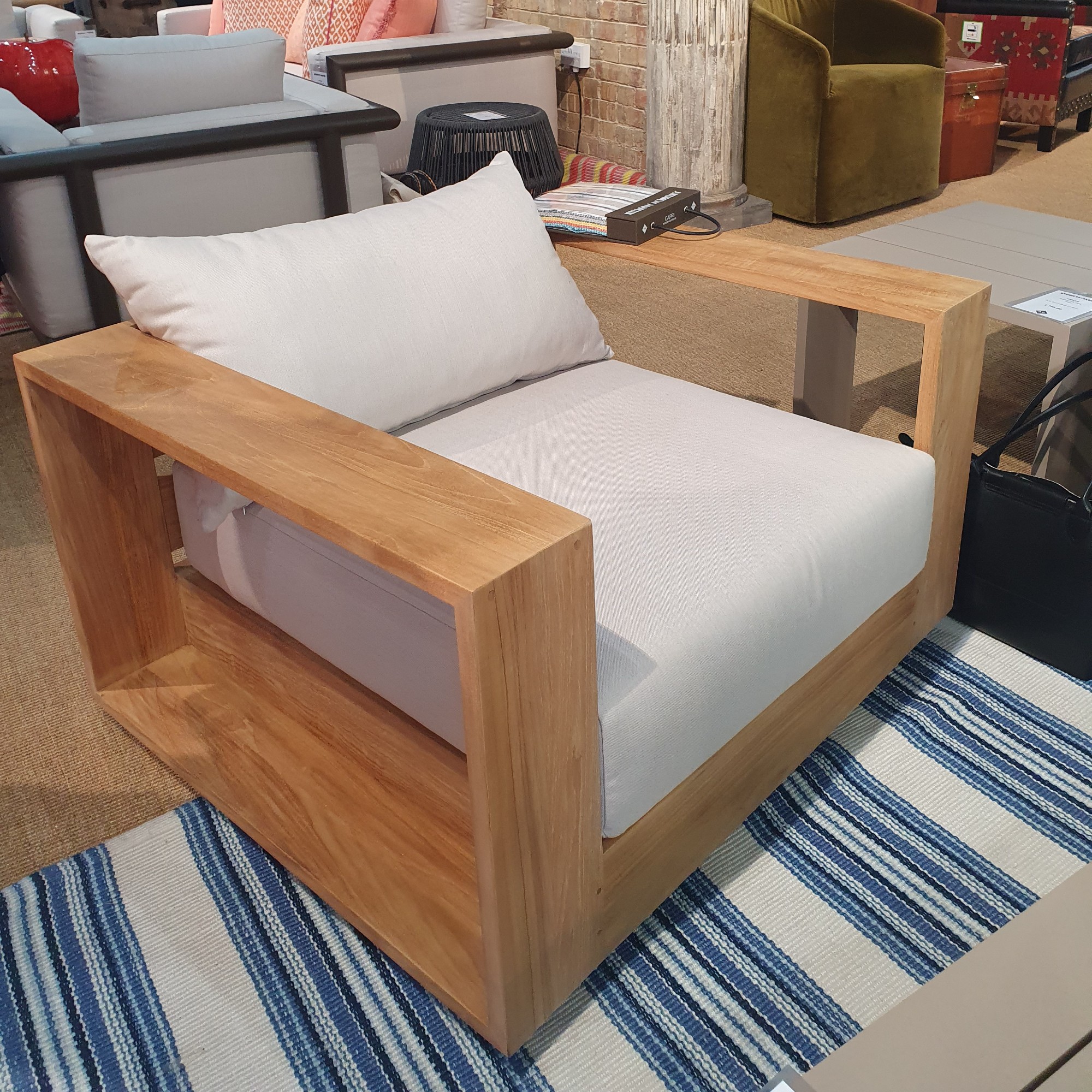 A garden swivel chair made with teak with cream cushions at the Andrew Martin showroom