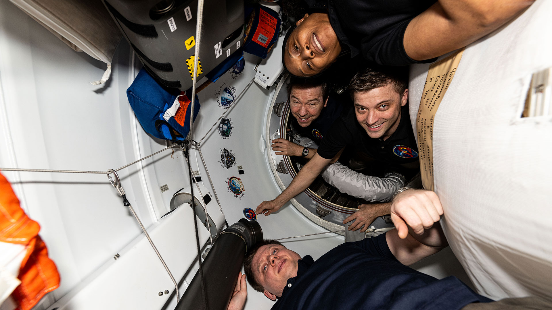 four astronauts squeezed into various corners of a spacecraft