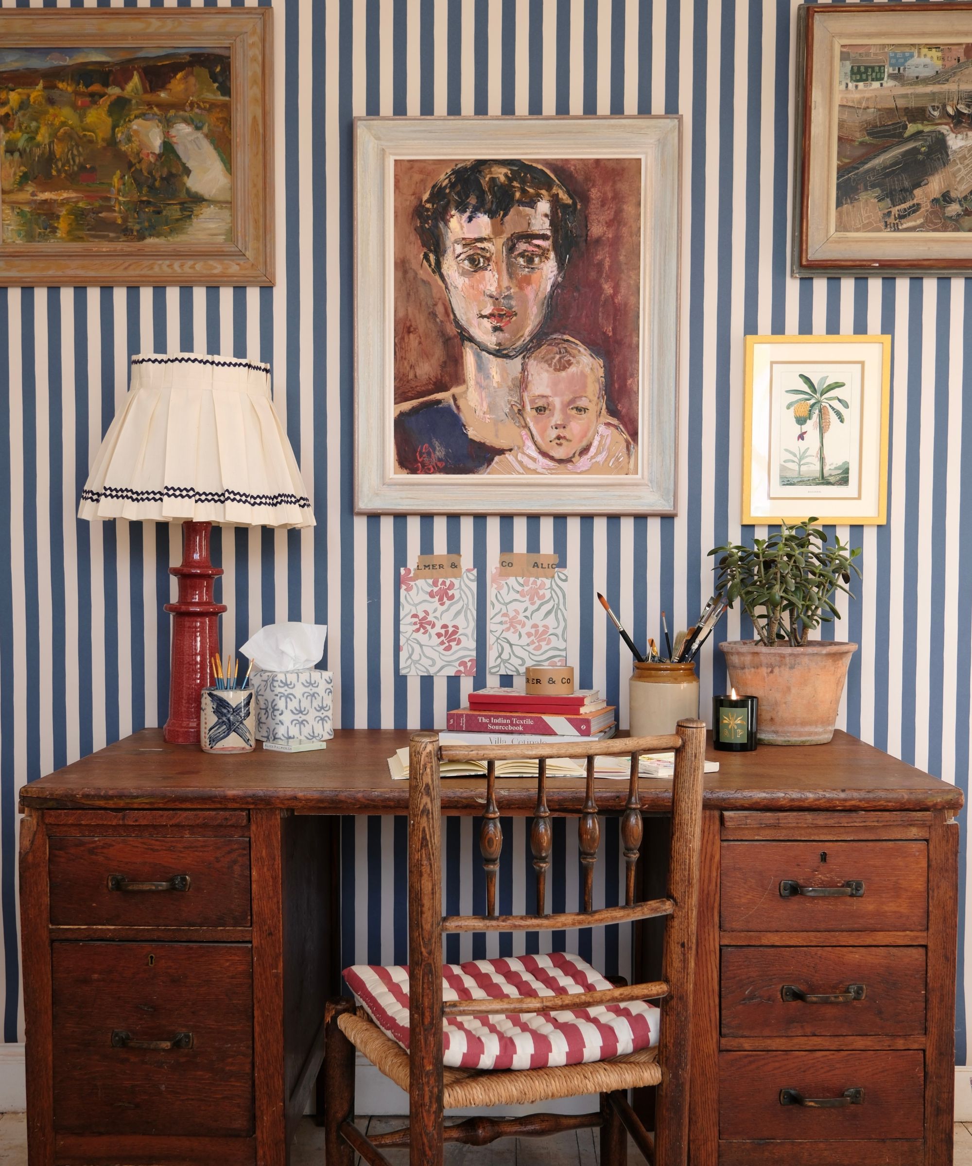 a home office with striped walls, an antique wooden desk, decor on the desk, and artwork hanging on the wall