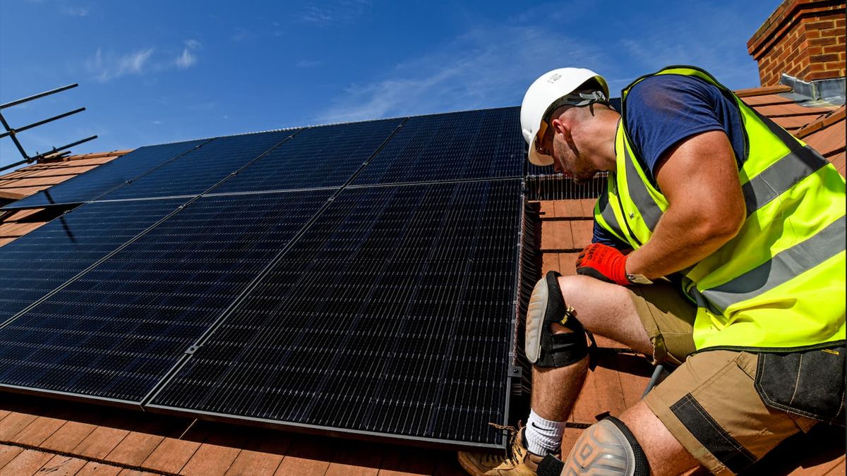 An EDF solar panel installer on top of a roof installing a solar panel