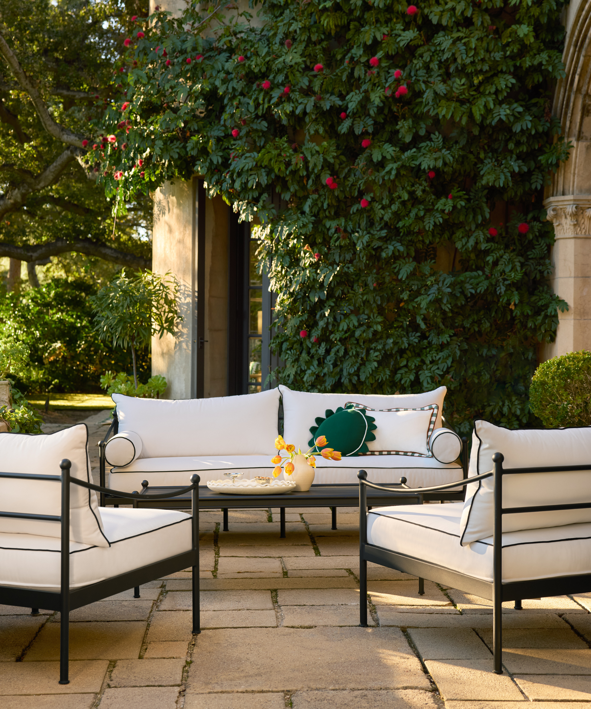 an outdoor patio with a couch and two accent chairs with white cushions, a metal coffee table, and decorative pillows