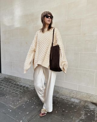 Woman weas knit jumper, satin trousers and brown suede bag